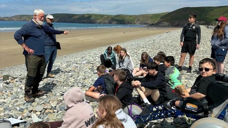 Young people on a beach listening to someone talk